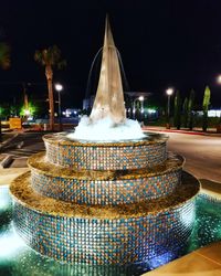 Illuminated fountain by building in city at night