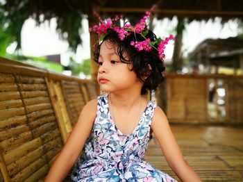 Thoughtful girl wearing flowers while sitting by bamboo railing
