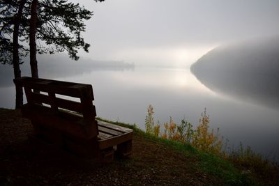 Bench by lake against sky