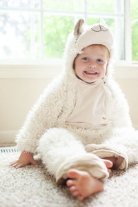 Portrait of happy young boy in llama costume sitting on floor at home