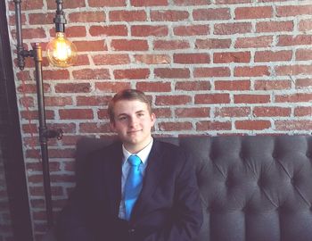 Smiling young man siting on sofa against brick wall