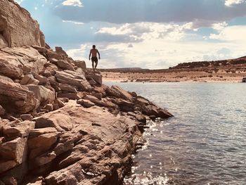 Man standing on rock by sea against sky