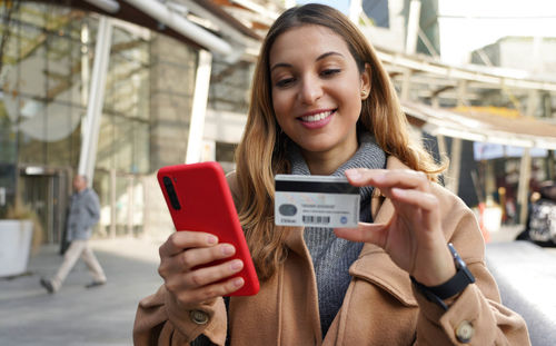 Happy smiling woman holding her smartphone and enters credit card number on winter season outdoors