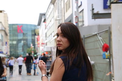 Rear view portrait of young woman on footpath in city