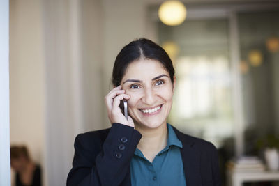 Smiling mid adult businesswoman talking on mobile phone in office