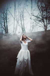 Female model standing in white evening gown at forest