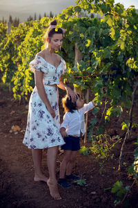 Family mother in a dress with her son walking through a vineyard in summer in italy