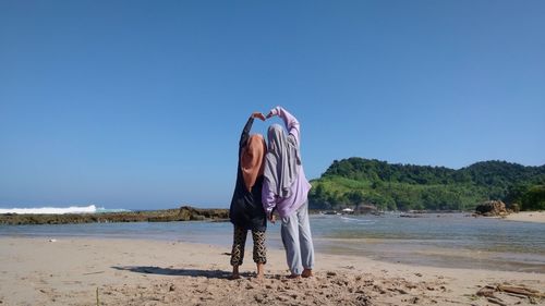 Rear view of woman standing at beach against clear blue sky