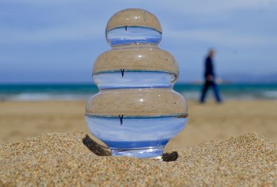 Close-up of glass container at beach against sky