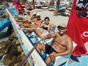 Portrait of people resting on chairs at beach during sunny day