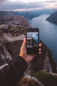 Hand holding smartphone with image of scene in background on it at norwegian fjords.