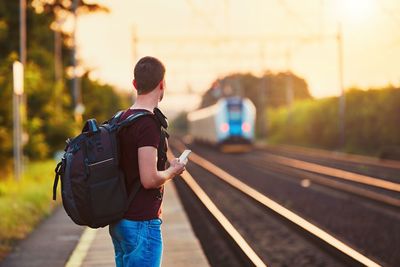 Side view of young man with backpack standing at railroad station platform