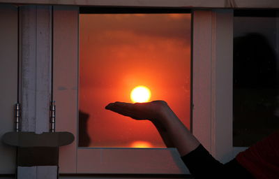 Person hand against window during sunset