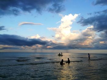 Silhouette people on sea against sky during sunset