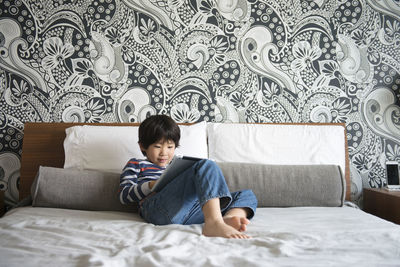 Boy sitting on bed and using digital tablet