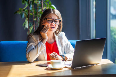 Young woman using mobile phone while sitting on table