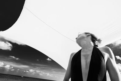 Low angle view of woman standing below parasol at beach