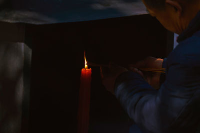 Man holding incense sticks over burning candle 