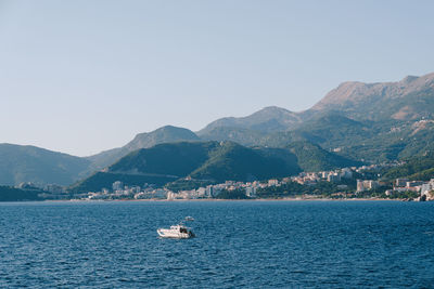 Sailboats sailing on sea by mountains against clear sky