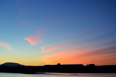 Silhouette building by sea against sky during sunset