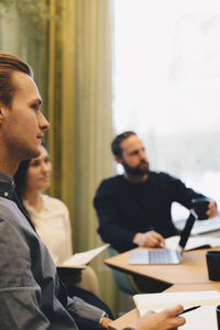 Side view of businessman sitting with colleagues in board room