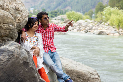 An indian couple sitting on rocks beside a river