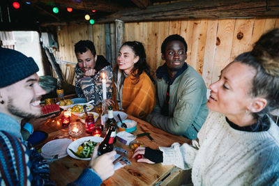 Male and female friends talking while having food on table in log cabin