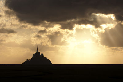 Silhouette of buddha statue against cloudy sky