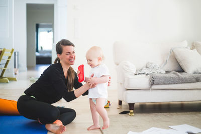 Cheerful working mother holding daughter while exercising in living room at home office