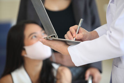 Midsection of doctor writing in clipboard while discussing with patient