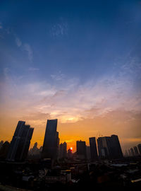 Silhouette buildings in city against sky during sunset