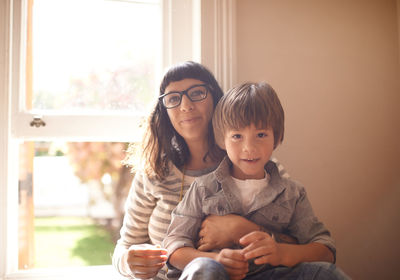Portrait of mother with boy sitting against window at home