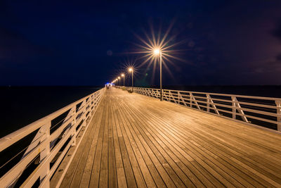 Illuminated jetty by sea against sky at night