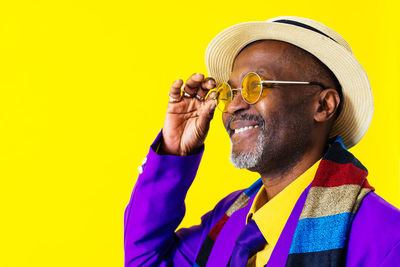 Smiling man holding eyeglasses against yellow background