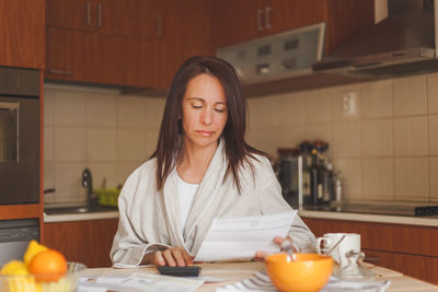 Woman reading document while having breakfast at home