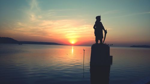 Silhouette statue by sea against sky during sunset