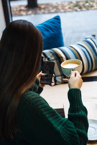 Woman enjoying coffee while browsing smartphone. a woman in a green sweater relaxes with a cup 