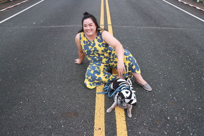 Portrait of smiling woman sitting with dog on road