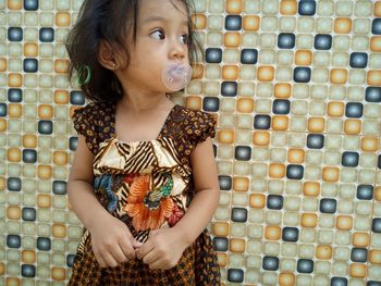 Girl with pacifier in mouth standing against wall