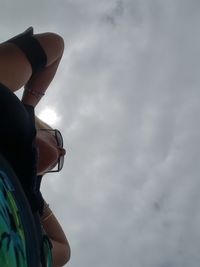 Low section of man riding woman standing against cloudy sky