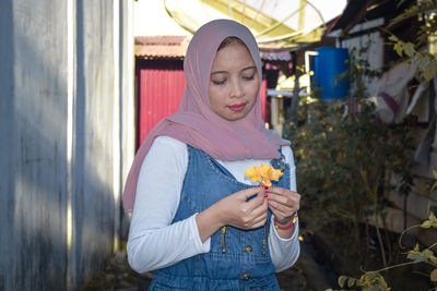 Full length of smiling young woman holding camera while standing outdoors