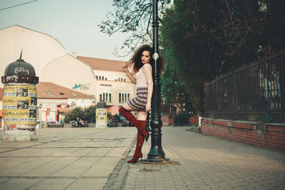 Side view portrait of young woman standing by pole in city