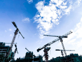 Low angle view of cranes at construction site against sky