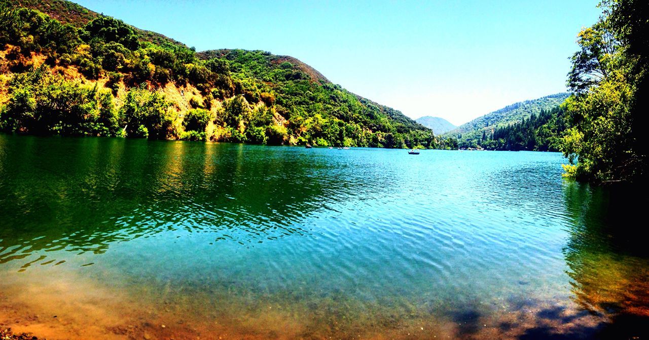 water, tranquil scene, scenics, clear sky, tranquility, mountain, beauty in nature, tree, lake, non-urban scene, nature, idyllic, growth, reflection, green color, blue, day, plant, remote, majestic, outdoors, mountain range, no people, waterfront, calm, tourism