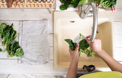 Healthy eating and dieting. young smiling woman in home clothes washing spinash in the kitchen