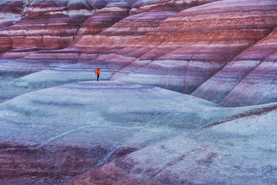 High angle of traveler in outerwear with backpack standing on top of smooth stone formation while exploring bentonite hills in utah, usa