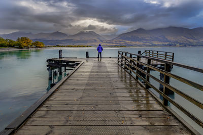 Rear view of man standing on pier over lake against sky