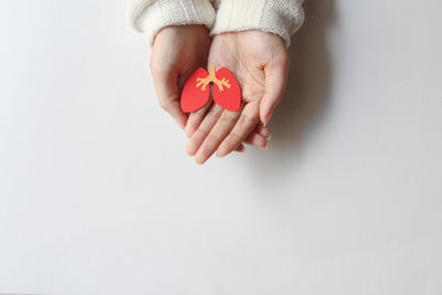 Cropped hand of woman holding orange fruit against white background