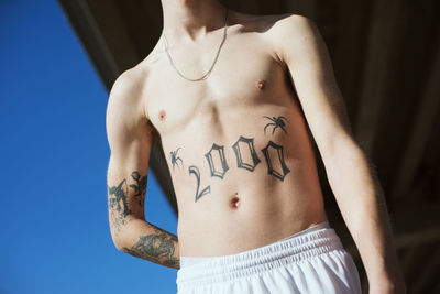 Low angle view of shirtless young man with tattoo standing outdoors