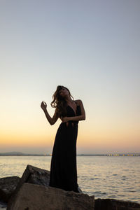 Woman standing by sea against sky during sunset